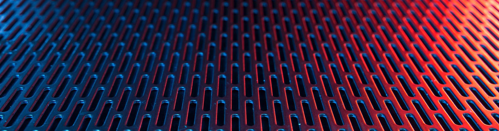 Photo of a sheet of slotted perforated metal with a red lighting over the right side of the sheet.