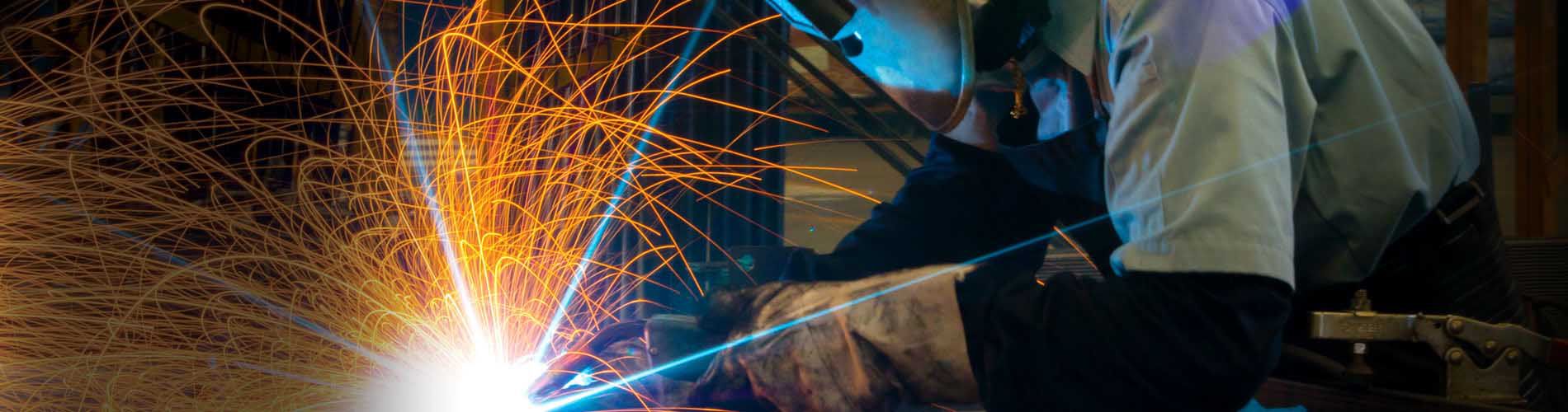 Image of a welder performing welding services, while the welding tool produces orange and blue light and sparks.